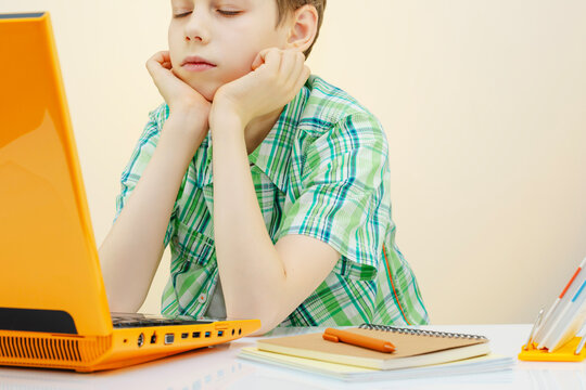 Bored Schoolboy Sitting At Desk With Laptop During Online Lesson. Concept of Distance Learning Fatigue, Student Motivation Challenge, Remote Education Reality, And Modern Digital School Life Visual
