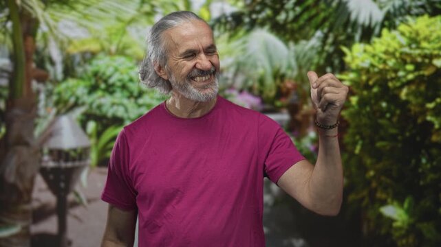 Man in magenta tshirt points index finger upward in forest with bare forearm visible; maturity contentment.