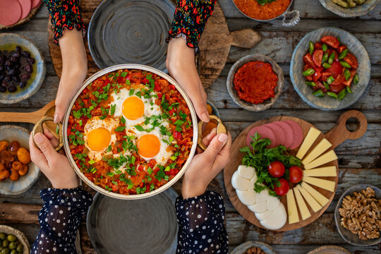 Scrambled eggs with tomato, pepper, onion and parsley named Menemen. Hands of two women sharing and holding their meal.  