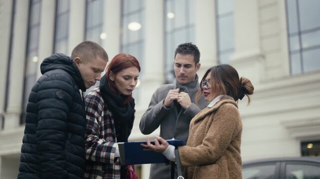 Four diverse business professionals engage in an outdoor meeting, reviewing and signing a document. A collaborative team discusses and finalizes an agreement in an urban setting.