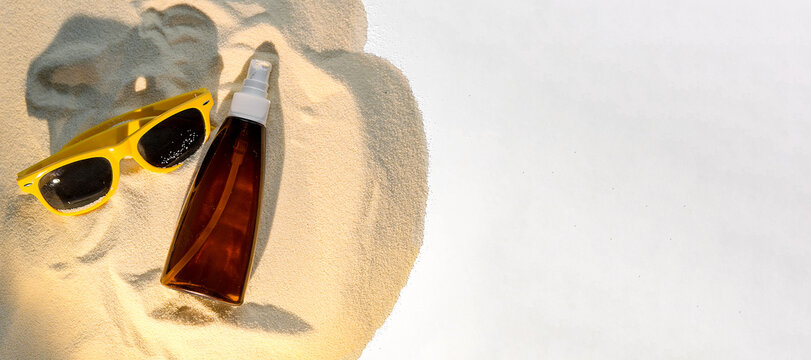Sunglasses and sunscreen bottle resting on sandy beach. Bright yellow sunglasses beside a brown sunscreen bottle. Summer relaxation concept.