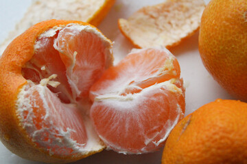 Partially peeled tangerine showing juicy orange segments with white membrane among whole citrus fruits on light background
