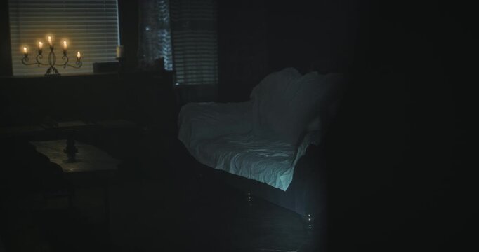 Shaky cam shot of flashlight shining on dark, empty living room with candles