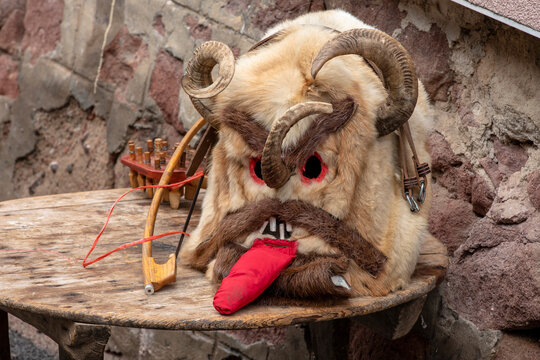 Traditional Bulgarian Kukeri mask made of animal fur and ram horns displayed on a wooden table.