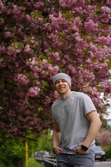 Smiling young man under blooming pink cherry tree in spring