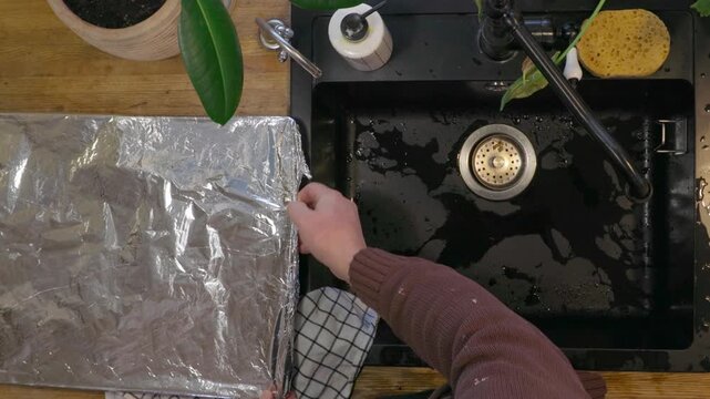 Top view of man cleaning and preparing fresh fish in black kitchen sink. Home seafood preparation process before cooking, everyday kitchen routine and food preparation concept