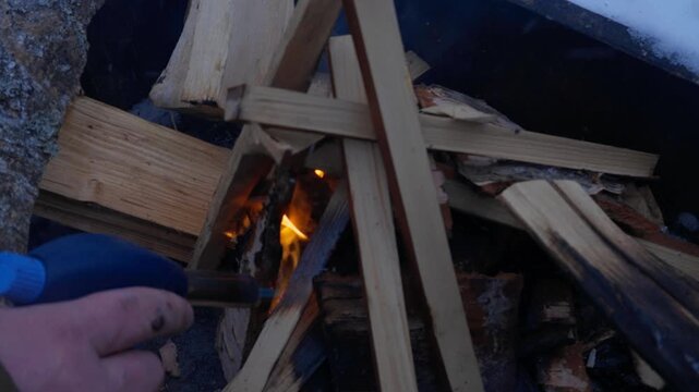 Person lighting firewood with gas torch in metal smoker outdoors in deep snow. Preparing wood fire for hot smoking fish during winter day. Traditional outdoor cooking and food preservation process