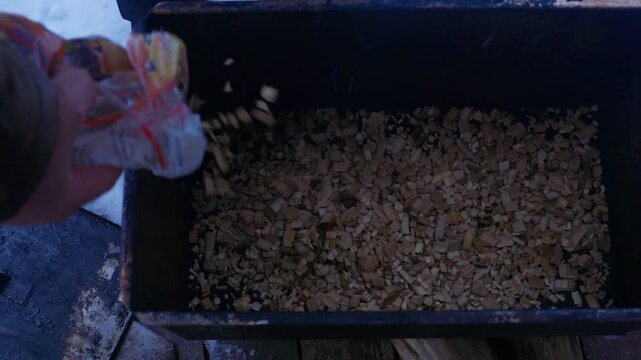 Fresh whole fish placed on grill rack inside metal smoker outdoors in winter. Preparing for hot smoking process in snowy conditions. Traditional outdoor cooking and fish preservation concept