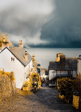 A view of a cobblestone street leading down to the sea, with buildings on either side and a dark, stormy sky overhead.