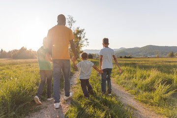 A father walks with his three children in a green field during sunset. They enjoy quality time outdoors sharing happy moments.