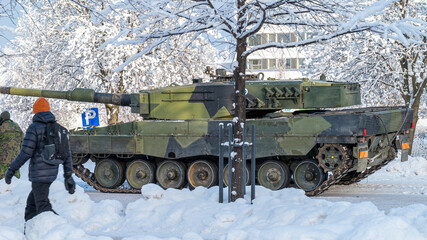Leopard 2A4 main battle tank in winter conditions. Heavy armored military vehicle on a snowy street. Arctic military equipment and urban background. © Amateur007