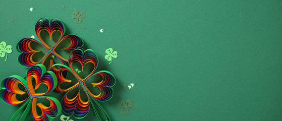 Panoramic wide banner with rainbow paper shamrocks on a green background. St Patrick's Day creative...