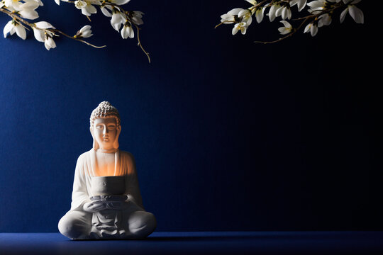 Buddha statue with candle on dark blue background decorated with flowers. Happy Vesak Day concept.