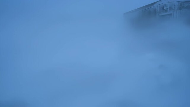 Industrial buildings and storage tanks at a remote arctic research station during a heavy snowstorm with low visibility and blue cold tones