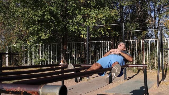 Athletic Middle Aged Man Doing Crunches on Parallel Bars - Calisthenics Park - Street Workout. Series Track Code: Fit-Mature-Man-54-Outdoor-Fitness-Series-2024