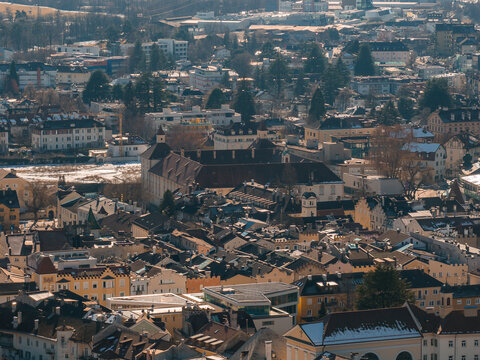 Aerial view of Brixen, Italy, shows pastel buildings, steep roofs, a large monastery complex, the Eisack River, snowy banks, evergreens, and long winter shadows.