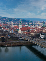 Aerial mid day winter view of Bratislava, Slovakia, showing St. Martin's Cathedral by the SNP Bridge over the Danube, red roofs, hills, cars and red buses in motion.