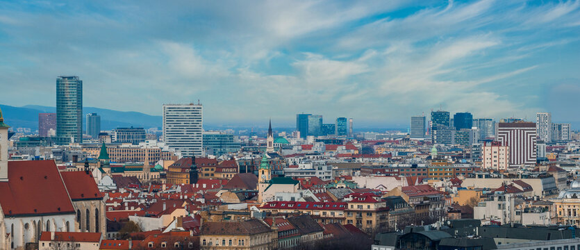 Bratislava, Slovakia, shows St. Martin's Cathedral spire and Eurovea and Nivy glass towers, with red roof historic blocks and Little Carpathians in calm daytime.