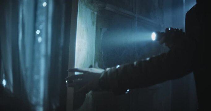 Closeup, handheld shot on woman's hand holding flashlight and quickly entering creepy room 