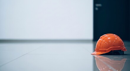 Orange safety hard hat helmet resting on clean reflective floor inside empty modern building corridor for construction industry and workplace safety concept with copy space