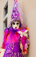 Obraz premium Venice, Italy - February 09, 2026: Colorful masked performer in elaborate purple costume with butterfly embellishments at Venice Carnival celebration near a historic building