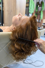 Fototapeta premium A woman relaxes in a beauty salon as her hair is styled. Soft curls frame her face, and the atmosphere is calm and inviting, perfect for pampering.