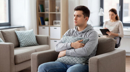 Obraz premium Young man attends therapy on sofa. Therapy session with counselor notes in background, therapy support for world mental health day, anxiety help, modern home office, calm concept, safe space