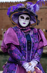 Obraz premium Venice, Italy - February 09, 2026: Woman in elaborate purple costume and mask poses during Venice Carnival, showcasing intricate details and vibrant colors against a historic backdrop