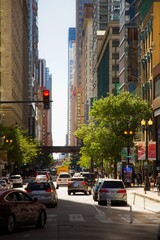 Fototapeta premium View of a Car Driving Down a Chicago Street at Sunrise with Tall Buildings Surrounding it