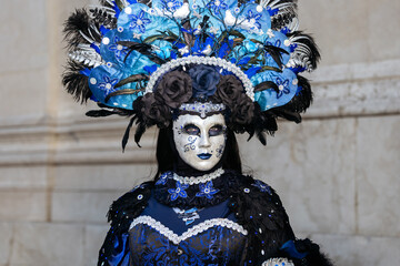 Obraz premium Venice, Italy - February 09, 2026: Woman in elaborate blue and black costume with feathered headdress and ornate mask at Venice Carnival in historical setting