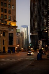 Obraz premium View of a Car Driving Down a Chicago Street at Sunrise with Tall Buildings Surrounding it