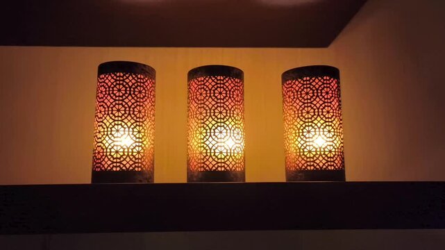 Three decorative candles in stylish candle holders glowing softly on a shelf in a spa environment. Warm dim light creates a serene, relaxing atmosphere associated with wellness, relaxation, and spa tr