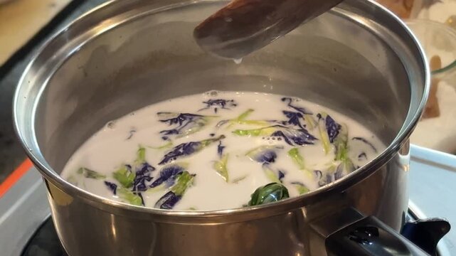 Stirring a Pot of Coconut Milk with Butterfly Pea Flowers to Make Thai Sticky Rice with Mango