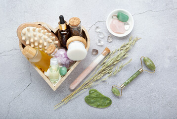 Holiday gift set for home spa with green jade roller, gua sha, facial oil, amber bottle, eco friendly packaging on gray stone background