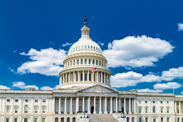 The US Capitol under a clear blue sky with clouds.