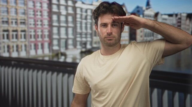 Man saluting with hand to forehead on street beside canal and gabled buildings in amsterdam; calm reflection.