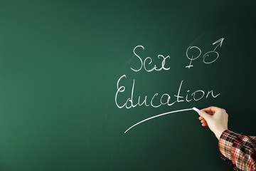 Woman writing words Sex Education on green chalkboard, closeup. Space for text
