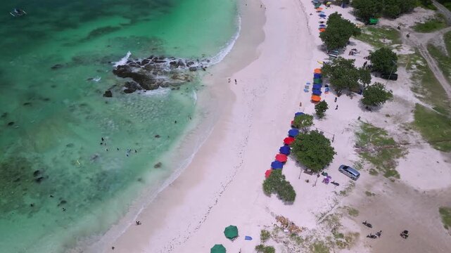 Aerial Cove Beach With Rocky Rockpool And Colorful Umbrellas On Curved Sand,Families Swimming Near Reef Patches,Lively Summer Energy And Clear Shallow Water,Tanjung Aan,Kuta,Lombok,Indonesia