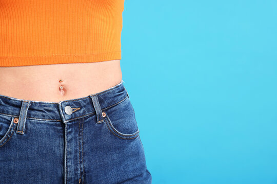 Woman with belly button piercing on light blue background, closeup. Space for text