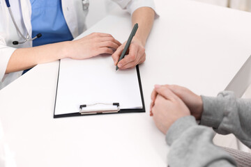 National health service (NHS). Woman having appointment with doctor at white desk indoors, closeup