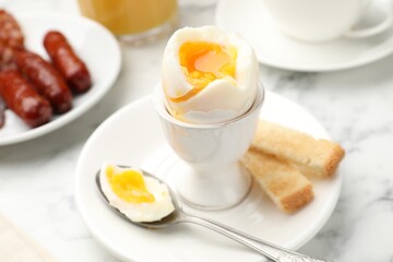 Tasty breakfast with soft boiled egg and toasted bread served on white marble table, closeup