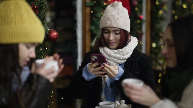 Three carefree girls gather for a festive coffee break in a winter setting. They chat and laugh while enjoying hot drinks outdoors during the holiday season.