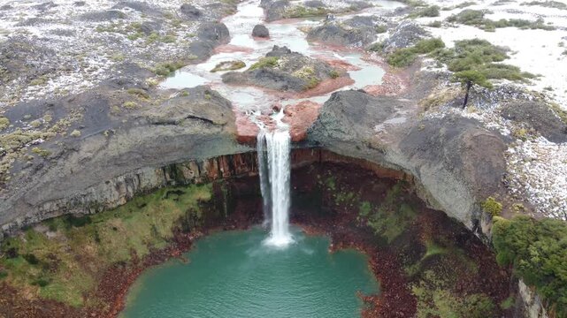 Drone view moving away from Salto del Agrio. Captures the waterfall dropping into a deep canyon with unique orange and yellow volcanic rock formations and basalt columns in the heart of Patagonia.