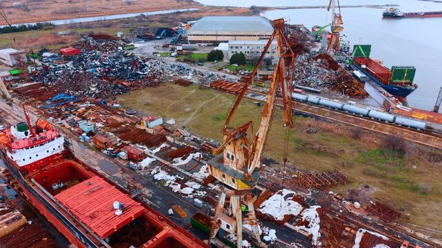 Rusty industrial cranes at shipyard near the water. Aerial view of heavy duty cranes and ship under repair at maritime facility.