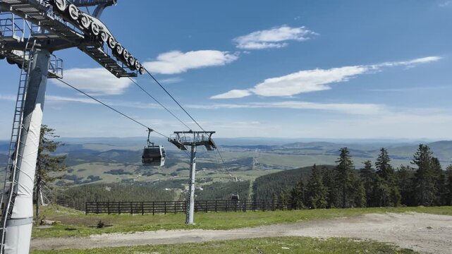 Cable car gondola in Zlatibor viewed from Tornik mountain with wide panorama of rolling hills and forest valley under blue sky. Scenic summer travel destination in Serbia