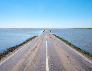 Road flooded and cut off with water crossing asphalt in rural area