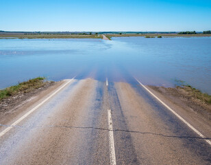 Road flooded and cut off with water crossing asphalt in rural area
