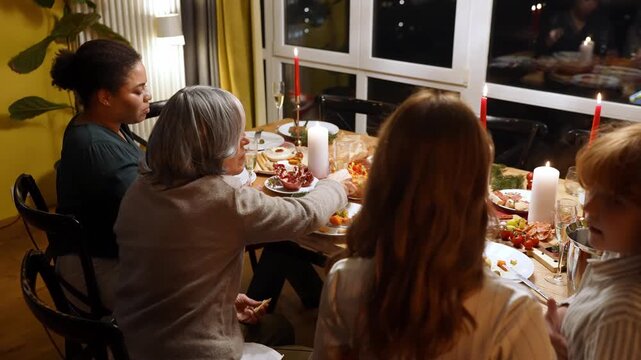 Mother sits at the table with her mother and female guest and hugs her daughter and son