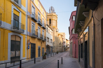 Narrow European street with yellow houses and old stone bell tower © Sergey