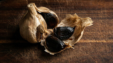 Fermented black garlic bulb partially peeled on rustic wood